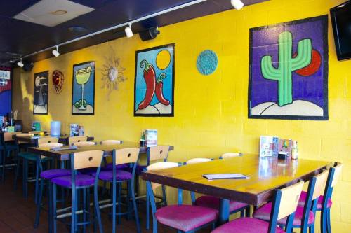 Colorful restaurant interior with yellow walls, vibrant artwork, and wooden tables and chairs.