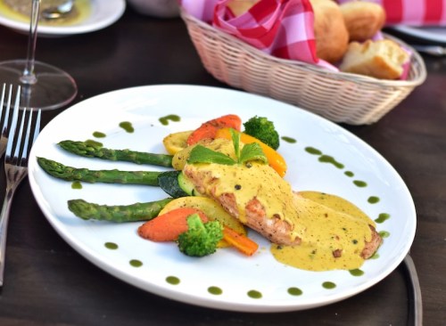 A plated dish featuring salmon with hollandaise sauce, asparagus, broccoli, and colorful vegetables on a white plate.