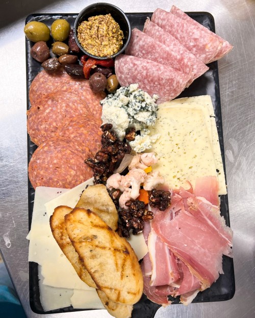 A charcuterie board featuring various meats, cheeses, olives, nuts, and mustard on a black platter.
