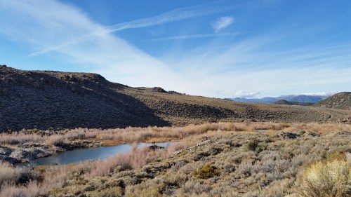 A serene landscape featuring a winding river, rocky hills, and sparse vegetation under a clear blue sky.