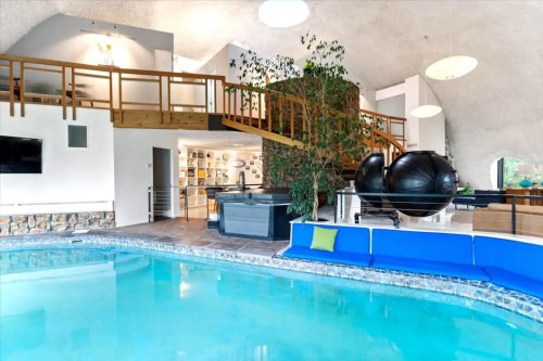 Indoor pool area featuring a blue couch, plants, and a lofted space with exercise equipment above.