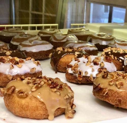 A variety of donuts with chocolate, white icing, and nut toppings displayed on a tray.