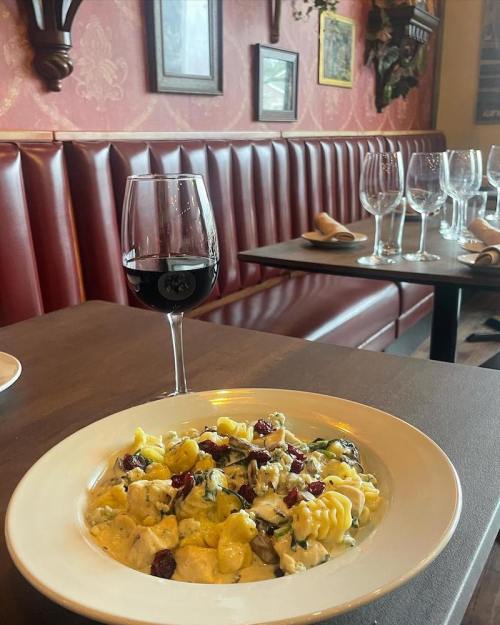 A plate of colorful pasta with spinach and cranberries, accompanied by a glass of red wine in a cozy restaurant setting.
