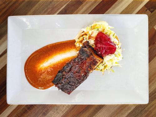 A plate featuring grilled meat with a rich sauce, accompanied by a fresh coleslaw and a dollop of red sauce.