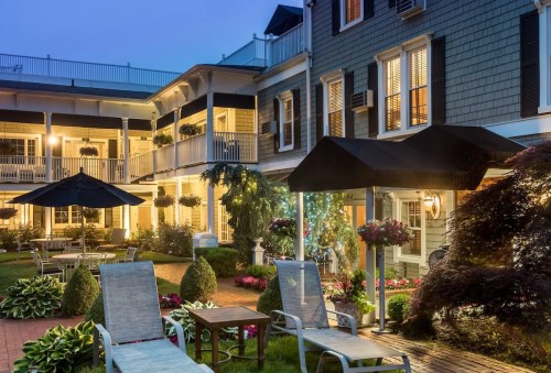 A cozy courtyard with lounge chairs, potted plants, and soft lighting in a charming building at dusk.