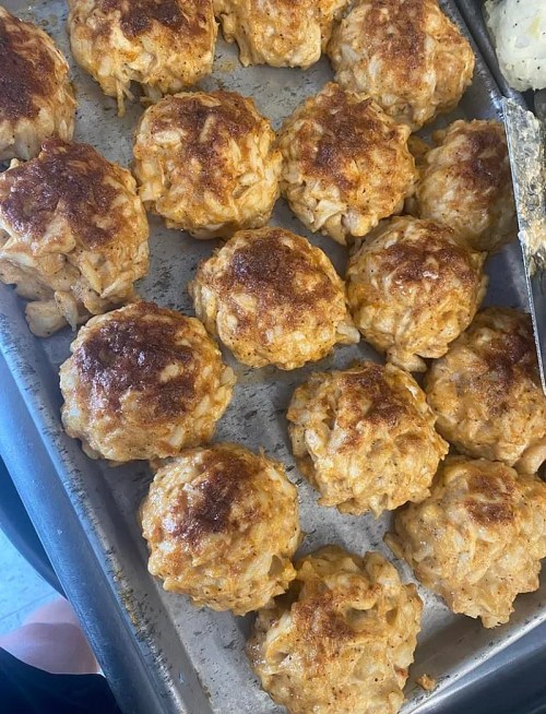 A tray of golden-brown, round crab cakes, freshly baked and arranged in neat rows.