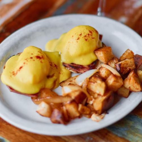 A plate of eggs Benedict topped with hollandaise sauce and a side of crispy, seasoned potato cubes.