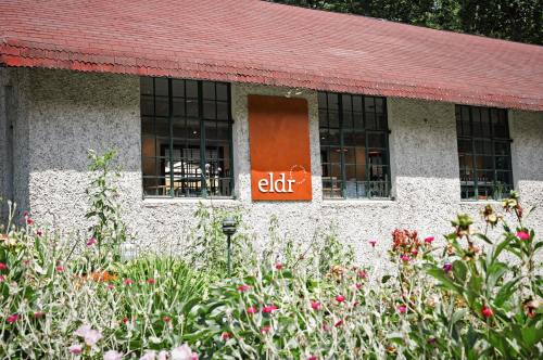 A building with a red roof and a sign reading "eldr," surrounded by colorful flowers in a garden.