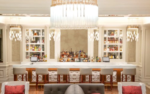 A stylish bar with a marble countertop, elegant lighting, and shelves filled with various bottles of liquor.
