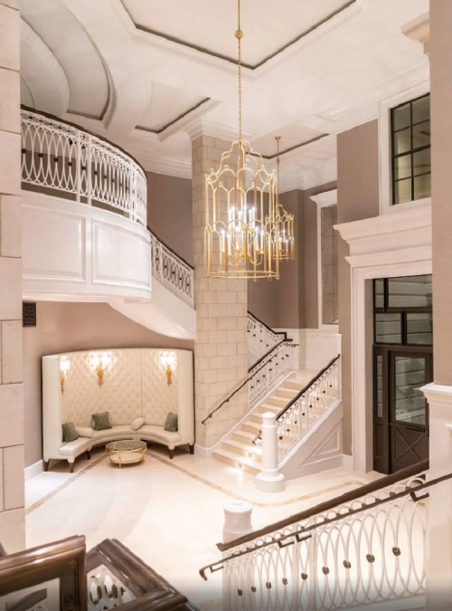 Elegant interior of a grand foyer featuring a staircase, decorative lighting, and plush seating.