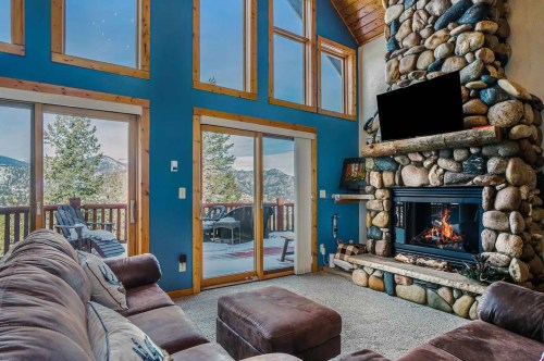 Cozy living room with a stone fireplace, large windows, and mountain views, featuring a comfortable sofa and ottoman.