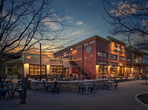 A cozy coffee shop with outdoor seating, illuminated by festive lights at dusk. Trees bare of leaves in the foreground.