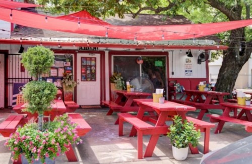 Outdoor dining area with red picnic tables, potted plants, and a canopy of red fabric over a small restaurant entrance.