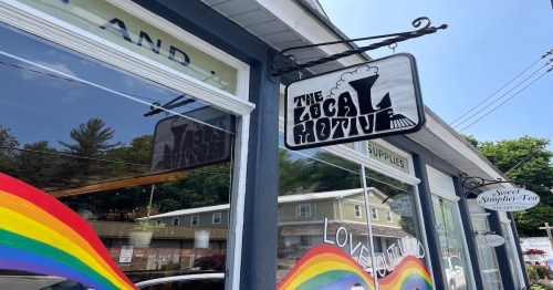 Sign for "The Local Motive" shop with a colorful rainbow mural on the window, showcasing a welcoming atmosphere.