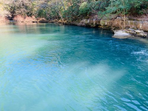 A serene river with clear turquoise water, surrounded by lush greenery and rocky banks.
