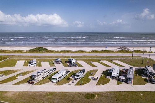 Aerial view of an RV park by the beach, with several RVs parked along a paved area near the ocean.