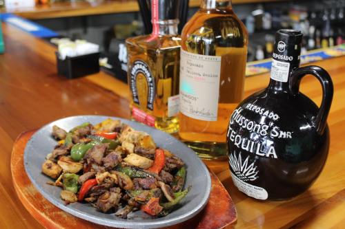 A sizzling platter of fajitas with grilled meat and vegetables, alongside bottles of tequila on a bar counter.
