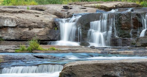 A serene waterfall cascading over rocks, surrounded by lush greenery and a clear blue pool below.