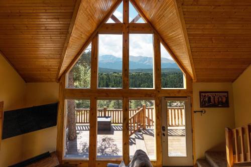 Cozy cabin interior with wooden beams, large windows showcasing mountain views and a deck outside.