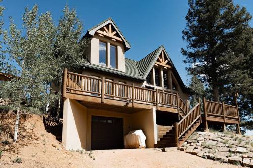 A modern house with a wooden deck, surrounded by trees, set on a hillside under a clear blue sky.