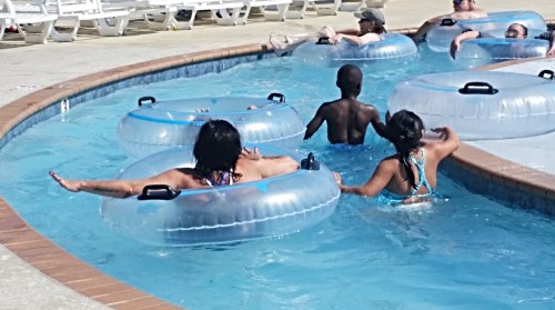 Children and adults relax in a pool on inflatable tubes, enjoying a sunny day.