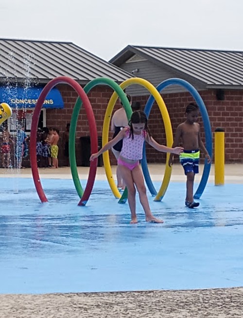 Children playing in a splash pad, running through colorful water arches on a sunny day.
