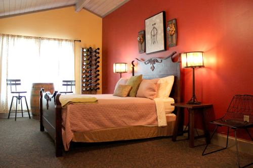 Cozy bedroom with a wooden bed, warm lighting, and a wine rack, featuring a red accent wall and a window with curtains.