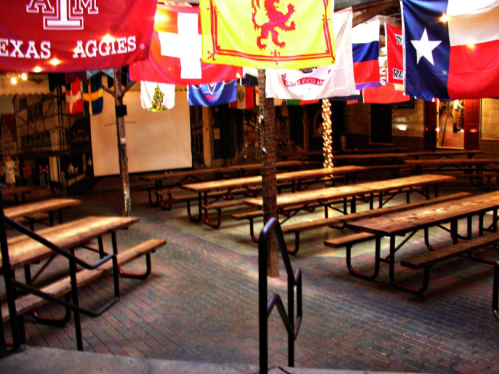 An empty indoor space with wooden picnic tables and colorful flags hanging from the ceiling.