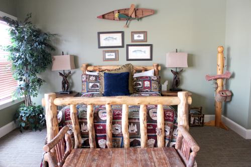 Cozy rustic bedroom with a log bed, fishing-themed decor, and a wooden bench in a warm, inviting color scheme.