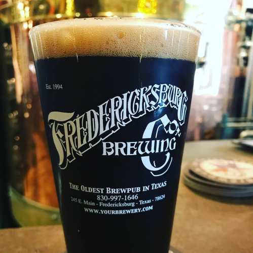 A pint of dark beer in a branded glass from Fredericksburg Brewing, showcasing the brewpub's logo and establishment year.