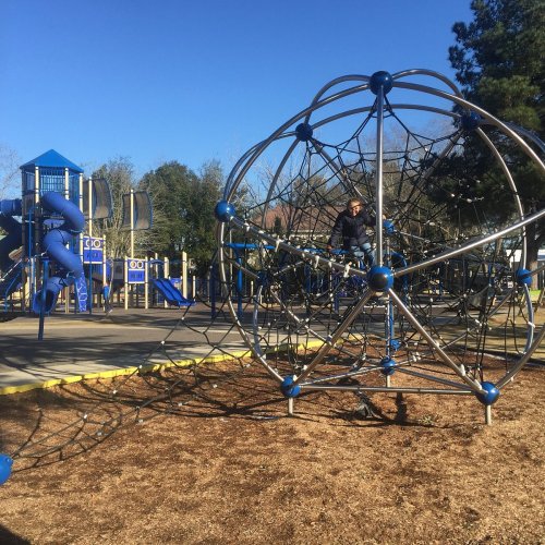 A playground with climbing structures and slides, featuring a large climbing web and a clear blue sky.