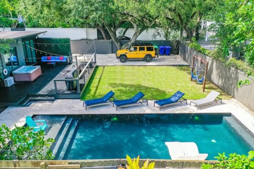 A backyard with a pool, lounge chairs, a grassy area, and a yellow SUV parked nearby under large trees.