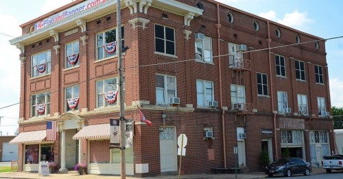Historic brick building with decorative banners, multiple windows, and air conditioning units on a sunny day.