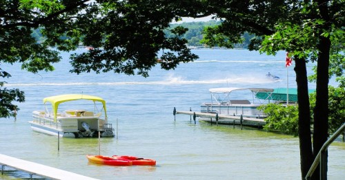 A serene lake scene with boats, kayaks, and trees, capturing a sunny day with water activities.
