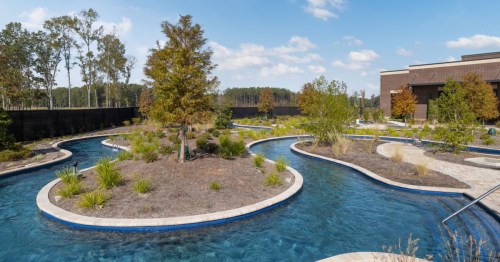 A winding waterway surrounded by landscaped greenery and trees under a clear blue sky.