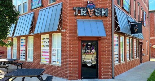 Exterior of a brick building with a sign reading "TRVSH," featuring large windows and outdoor seating.