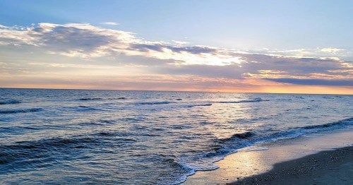 A serene beach scene at sunset, with gentle waves and a colorful sky reflecting on the water.