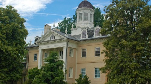 Historic mansion with a domed roof, surrounded by lush greenery and blue skies.