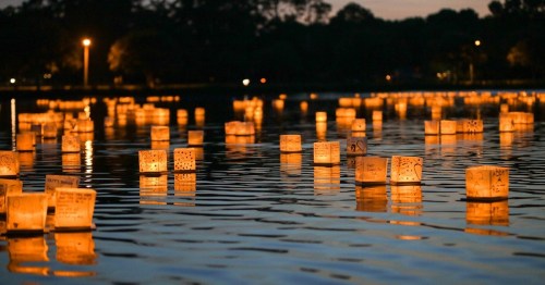 Floating lanterns illuminate a calm lake at dusk, reflecting warm light on the water's surface.