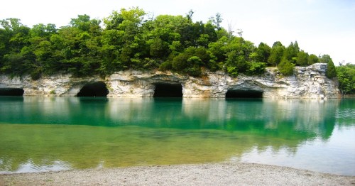 A serene lake with clear turquoise water reflecting rocky cliffs and lush greenery along the shore.