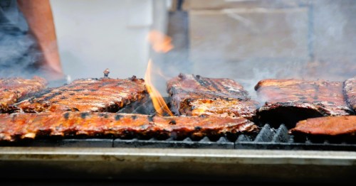 Grilled ribs sizzling on a barbecue, surrounded by smoke and flames.