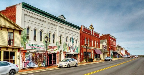 Historic buildings line a street, featuring shops and restaurants with colorful murals and awnings.