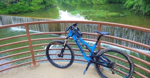 A blue mountain bike rests on a bridge overlooking a serene waterfall and lush green surroundings.