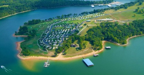Aerial view of a lakeside campground with green spaces, docks, and recreational areas surrounded by water and trees.
