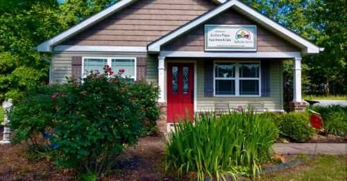 A charming house with a red door, surrounded by greenery and flowers, featuring a sign for "Sallie's Place."