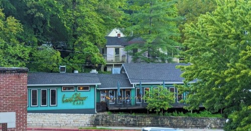 A cozy café nestled among lush green trees and hills, featuring large windows and a welcoming exterior.