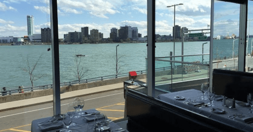 View from a restaurant window overlooking a river, city skyline, and a boat on the water under a partly cloudy sky.