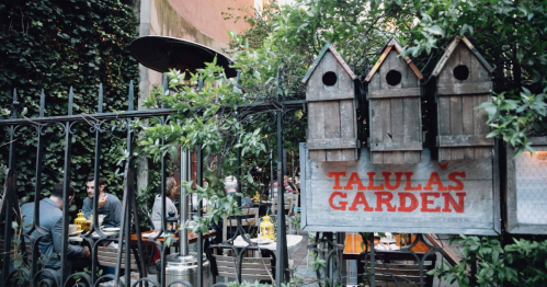 A cozy outdoor dining area with a sign reading "Talula's Garden" surrounded by greenery and patrons enjoying their meals.