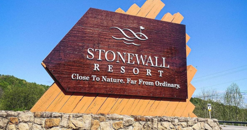 Sign for Stonewall Resort, featuring a wooden design with the slogan "Close To Nature. Far From Ordinary." against a blue sky.