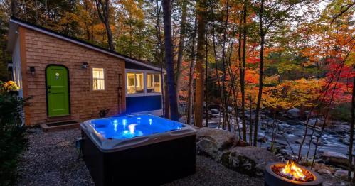 Cozy cabin by a river, featuring a hot tub and a fire pit, surrounded by vibrant autumn foliage.